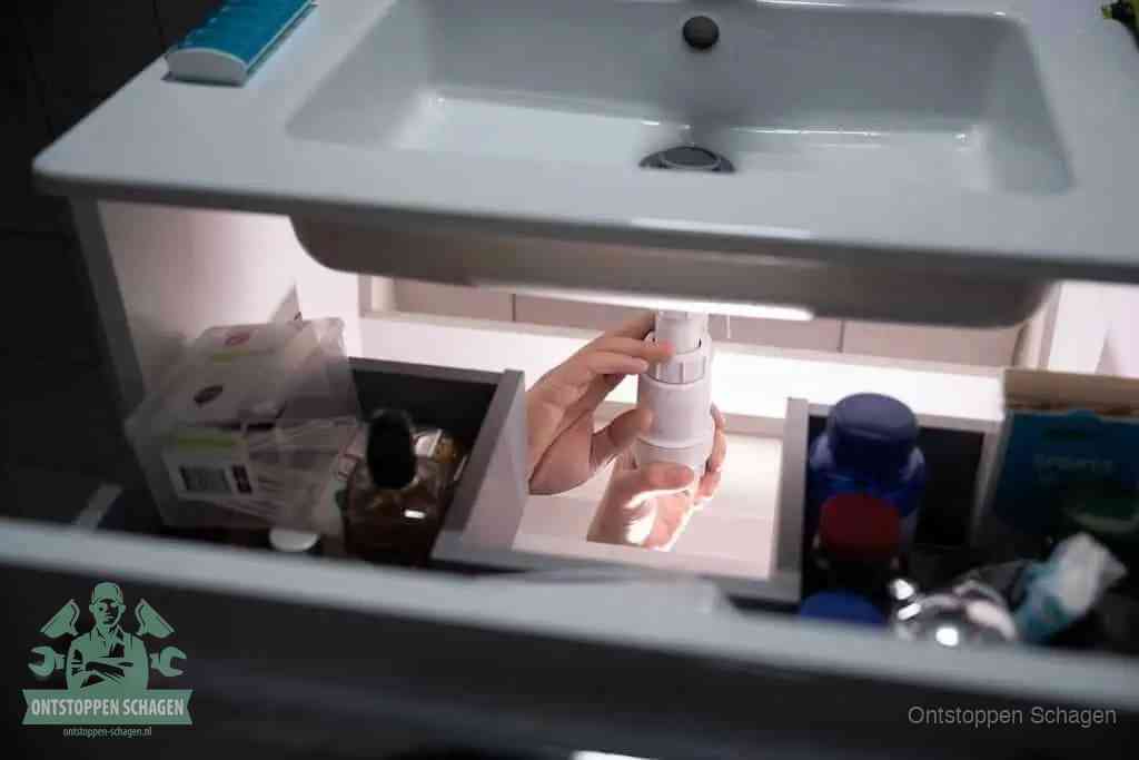 Een pompfles met zeep boven een wastafel, de heet water en afwasmiddel-methode om een vetprop in de afvoer los te maken in Schagen