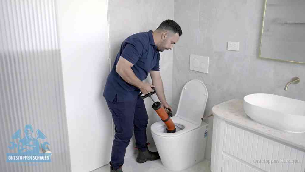 Een monteur buigt over een wandcloset en duwt met de hand een persluchtontstopper in de toiletpot om de verstopping handmatig los te maken in Schagen