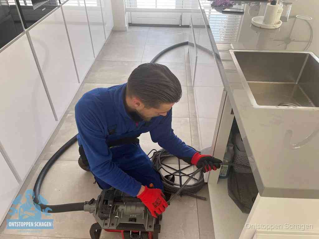 Een monteur ontstopt de keukenafvoer onder de spoelbak met een elektrische veermachine in Schagen