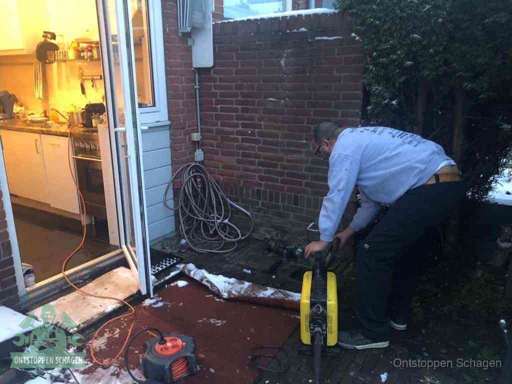 Een monteur werkt buiten bij een open riool-/grondput met een elektrische ontstoppingsmachine om een verborgen afvoerprobleem op te sporen in Schagen