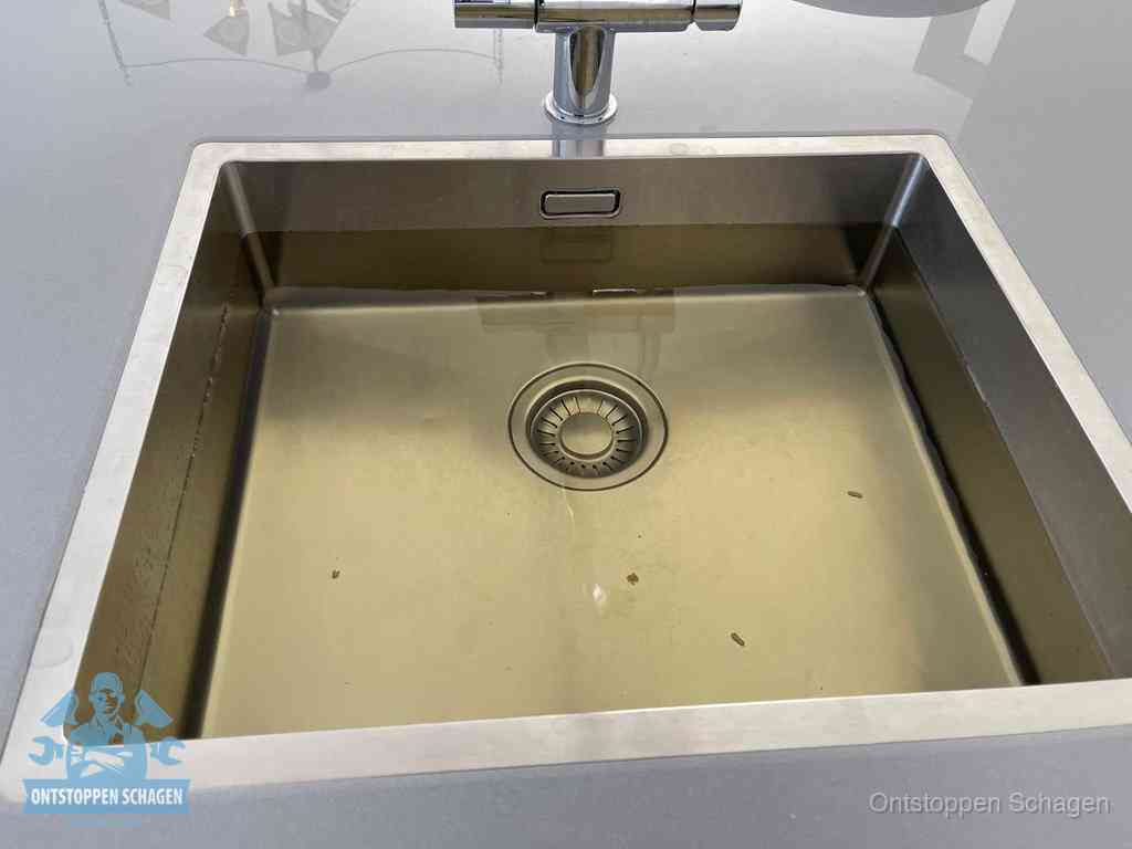 Stilstaand water in een rvs spoelbak dat niet wegloopt, een duidelijk signaal van een gootsteenverstopping in Schagen