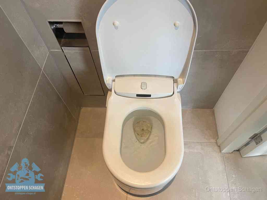 Een wit hangtoilet waarin een prop wc-papier op het water blijft drijven, een duidelijk signaal van een verstopte wc in Schagen