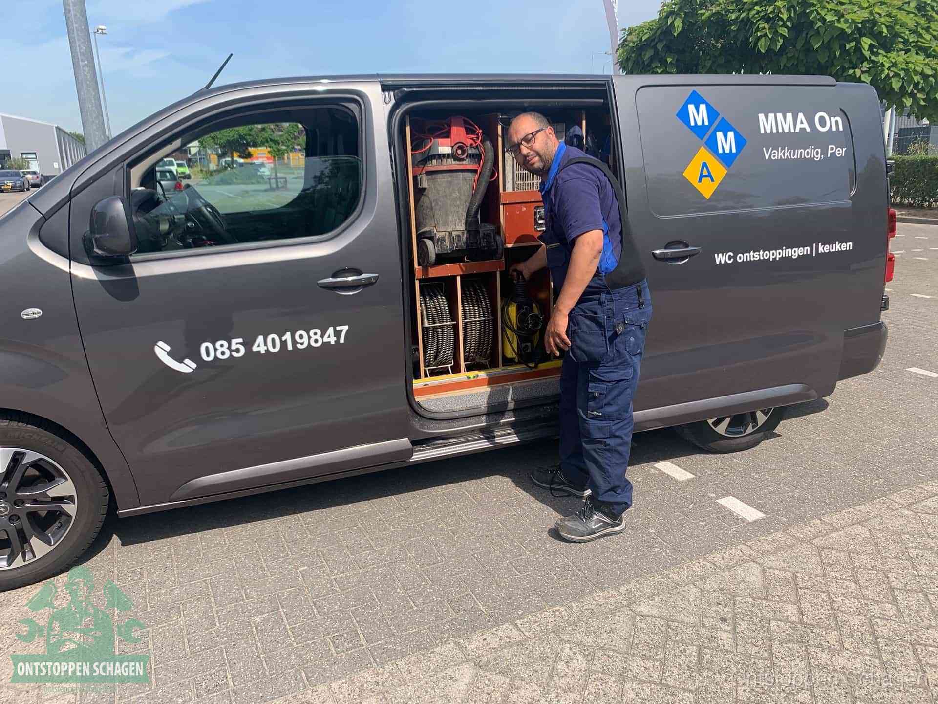 Een monteur bij de open schuifdeur van zijn bedrijfsbus op een parkeerplaats, klaar om de oorzaak van terugkerende afvoerverstoppingen aan te pakken in Schagen