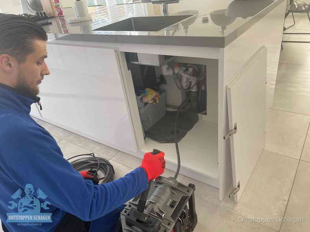 Monteur ontstopt met een veermachine een verstopte afvoer onder de gootsteen in Schagen