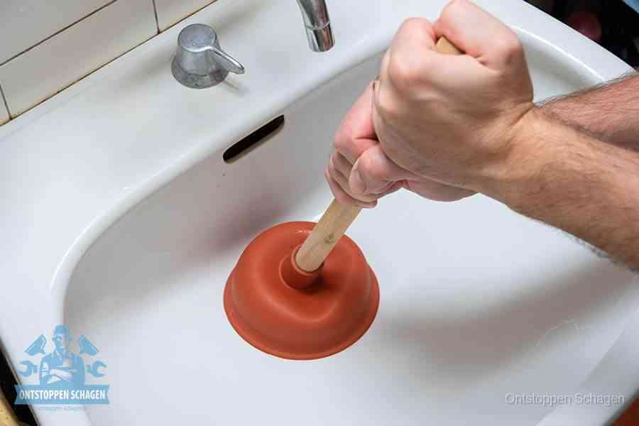 Twee handen gebruiken een rode rubberen plopper op een sanitair-afvoer om het toilet te ontstoppen in Schagen