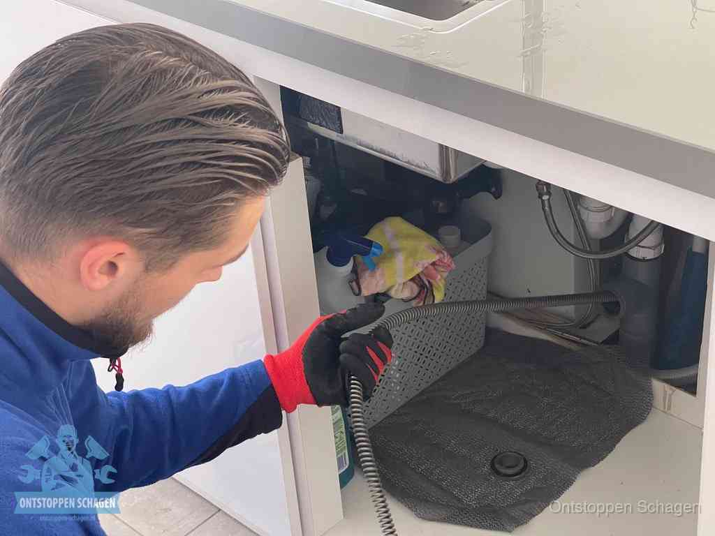 Een monteur voert een flexibele ontstoppingsveer in de afvoer om een verstopping voorbij de bocht van het toilet te bereiken in Schagen