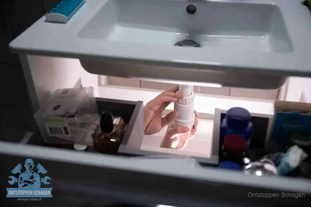 Een pompfles met zeep boven een wastafel in de toiletruimte, de warm water en afwasmiddel-methode om de wc te ontstoppen in Schagen