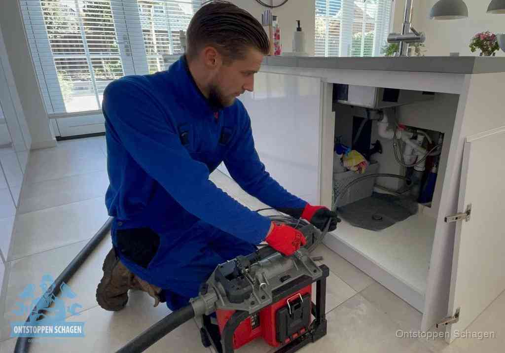 Een monteur voert een professionele elektrische ontstoppingsmachine in de afvoer onder de spoelbak tijdens het gootsteen ontstoppen in Schagen